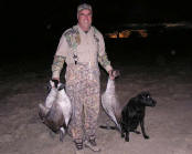 Picture of hunter with three geese and his dog.